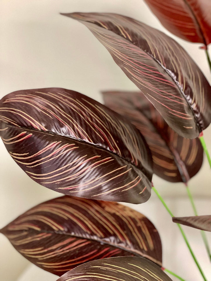 Close-up of artificial dark red and brown tropical leaves with detailed veining, bringing a vibrant and exotic flair to any indoor setting.