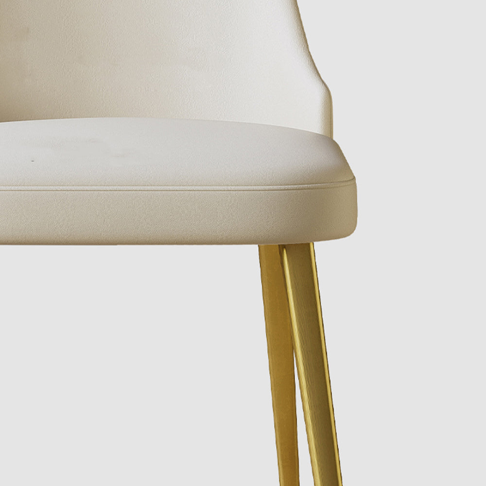 Close-up of a sleek cream dining chair with gold metal legs, showcasing its soft cushion and modern design. Frequently asked questions include 'What is the most comfortable material for dining chair seats?' and 'How durable are gold metal legs on dining chairs?