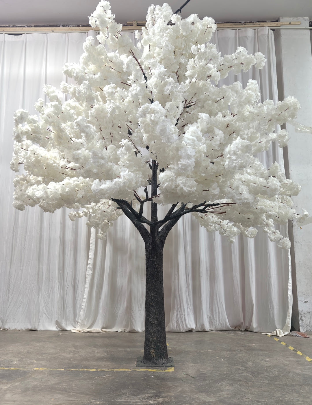 A tall artificial white blossom tree with a sturdy base, displayed against a plain white backdrop. Suitable for indoor event decor and photo backdrops. How durable are the materials used for these artificial trees?