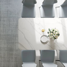 Charger l&#39;image dans la galerie, Modern white marble dining table surrounded by gray upholstered chairs in a contemporary dining room setting. The table features a vase with white flowers and a small bowl, showcasing a minimalist yet elegant design
