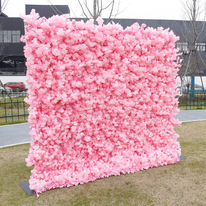 Large pink artificial flower wall backdrop set up outdoors, commonly used for events like weddings, parties, and photoshoots. Is this flower wall backdrop weather-resistant? How easy is it to assemble and transport? Can it be customized in other colors?