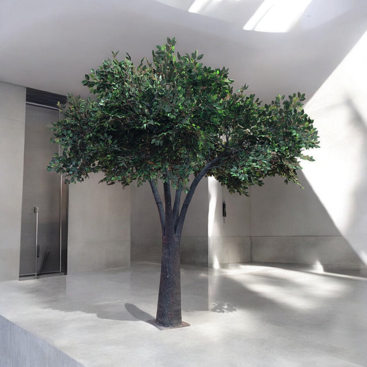 Artificial tree with a lifelike trunk and lush green foliage, positioned in a minimalist indoor venue, perfect for adding a natural touch to modern wedding and event decor. Can these rental trees be used to create a focal point for event photography?