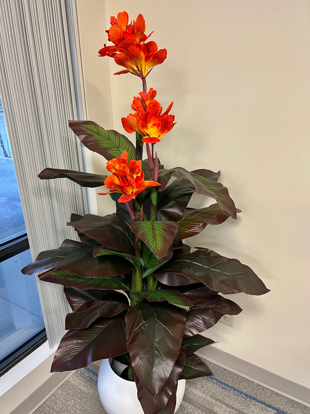 Artificial tropical canna lily plant with vivid orange flowers and broad, dark green leaves, displayed in a sleek white planter.