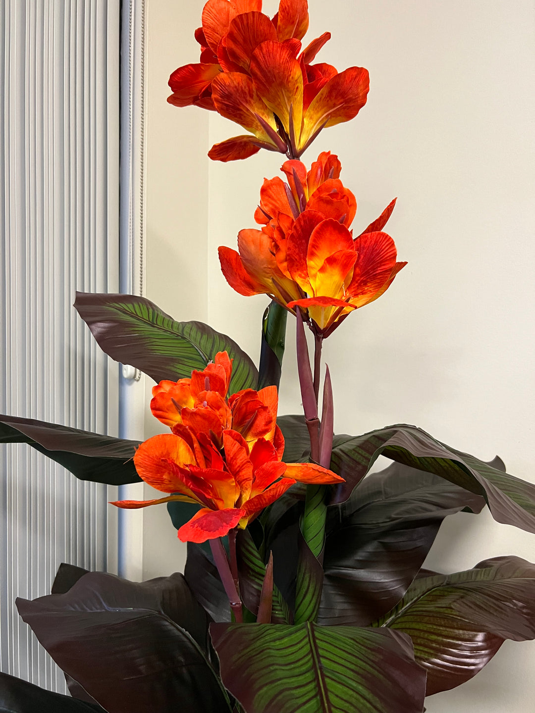 Artificial tropical canna lily plant with striking orange flowers and deep green leaves with detailed veining, creating a vibrant and exotic accent for indoor decor.