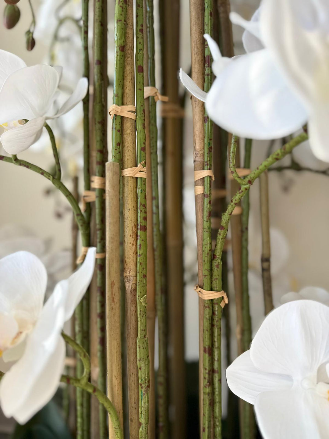White orchids with realistic green stems and brown tape on a blurred background.
