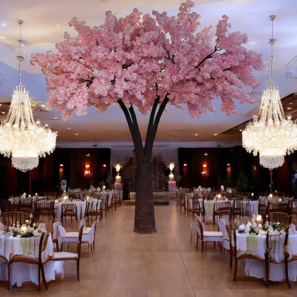 Luxurious artificial tree with vibrant pink blossoms, serving as a centerpiece in an opulent banquet hall adorned with sparkling chandeliers and elegantly set round tables. Can these rental trees create a fairy-tale ambiance for weddings and special events?