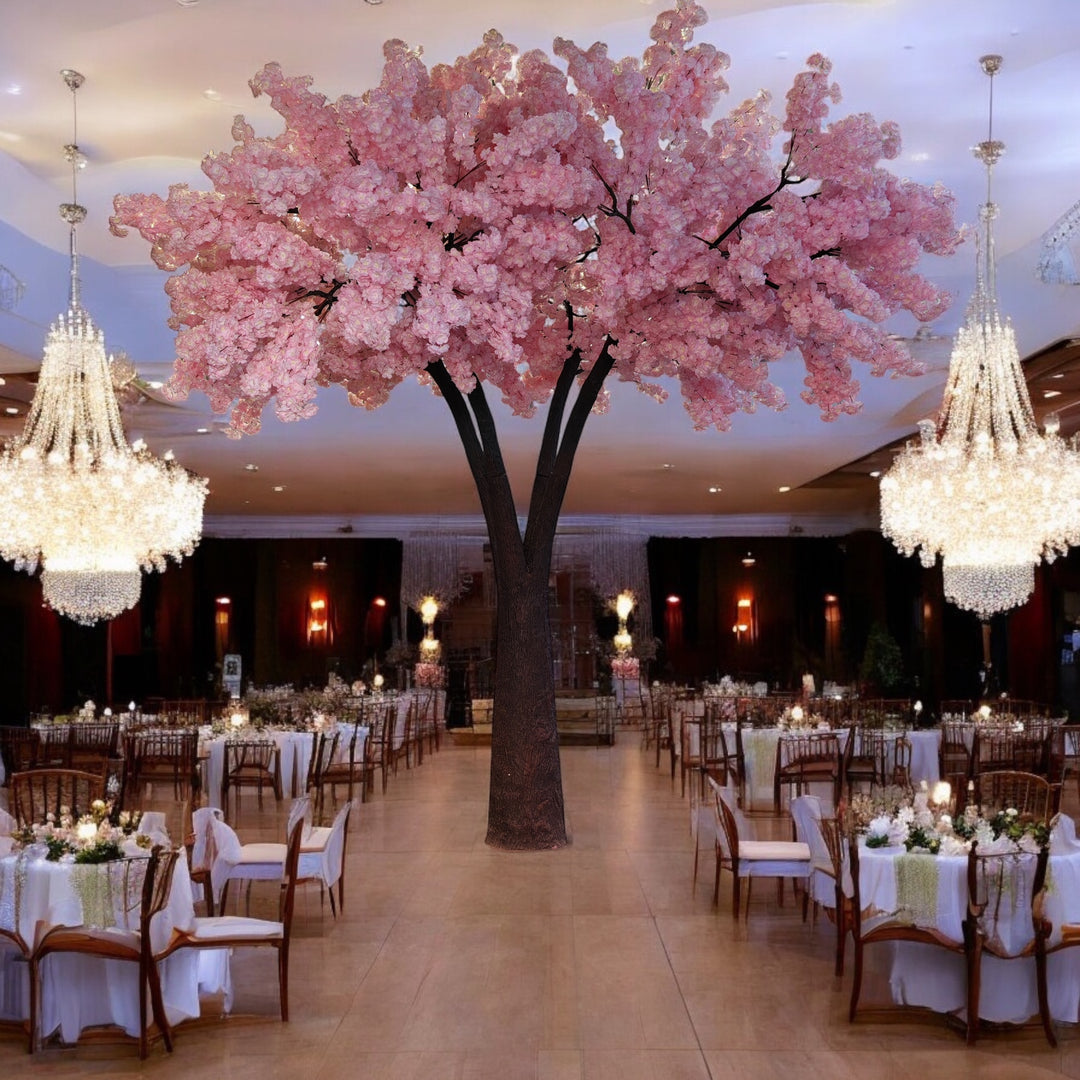 Luxurious artificial tree with vibrant pink blossoms, serving as a centerpiece in an opulent banquet hall adorned with sparkling chandeliers and elegantly set round tables. Can these rental trees create a fairy-tale ambiance for weddings and special events?