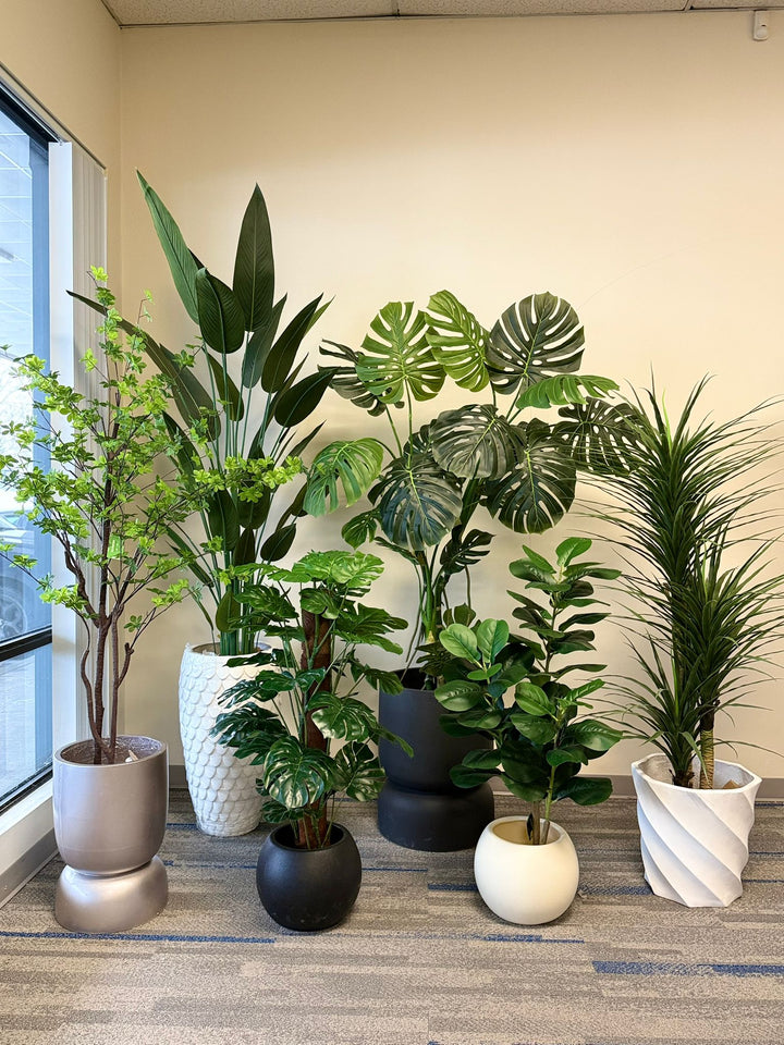 Collection of potted artificial tropical plants on a carpeted floor near a window