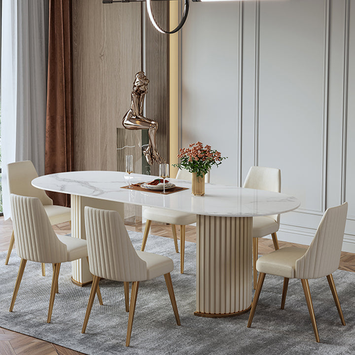 Luxurious round marble-top dining table with golden legs, paired with plush cream-upholstered chairs featuring vertical channel tufting and gold-toned legs, set on a soft gray rug in an elegant, light-filled room.