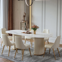 Load image into Gallery viewer, Luxurious round marble-top dining table with golden legs, paired with plush cream-upholstered chairs featuring vertical channel tufting and gold-toned legs, set on a soft gray rug in an elegant, light-filled room.
