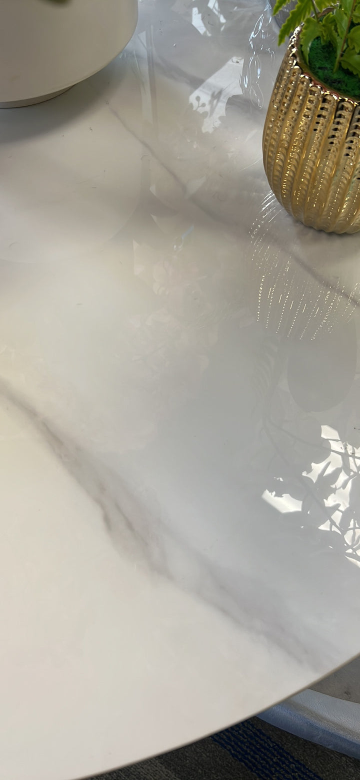 Close-up of a glossy white marble tabletop with subtle gray veining, featuring a gold decorative planter, highlighting the smooth, elegant finish of the marble surface