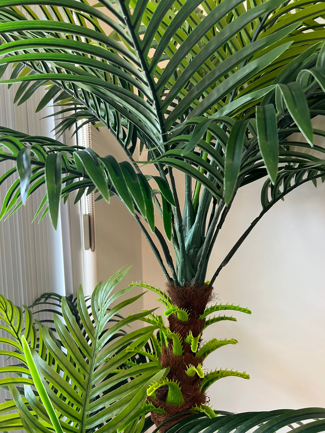 Artificial palm tree with detailed close-up of lush green fronds and a realistic trunk base, perfect for home or office decoration.