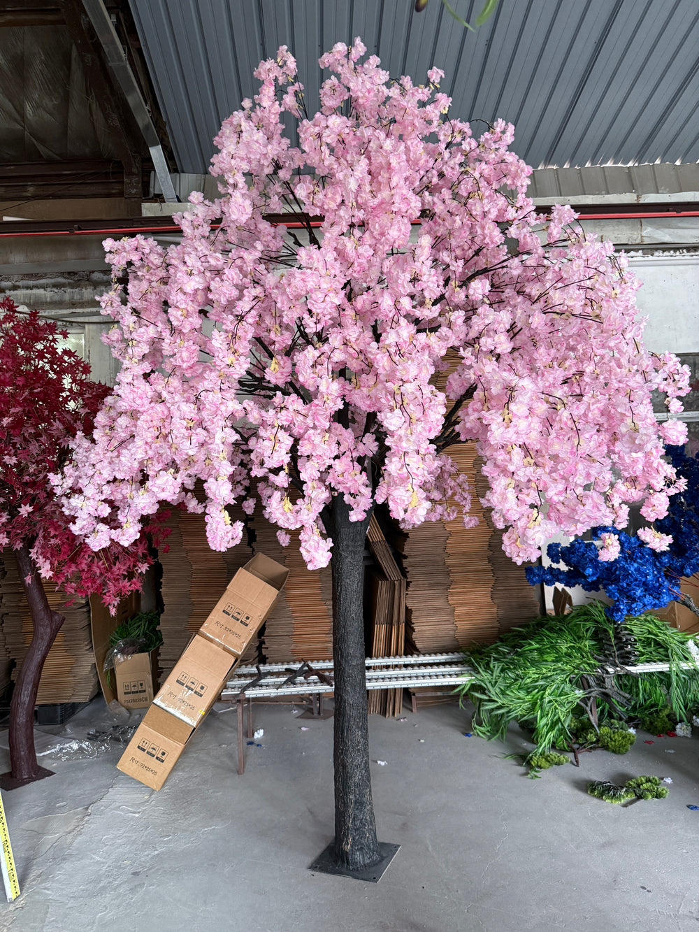 Pink floral arrangement in a pot on a gray concrete floor with boxes and plants in the background stored in a warehouse.