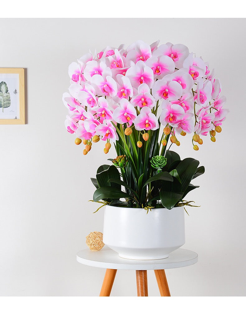 A stunning arrangement of artificial pink and white orchids displayed in a white round pot, placed in a showroom setting. How can I incorporate artificial orchids into modern interior design?