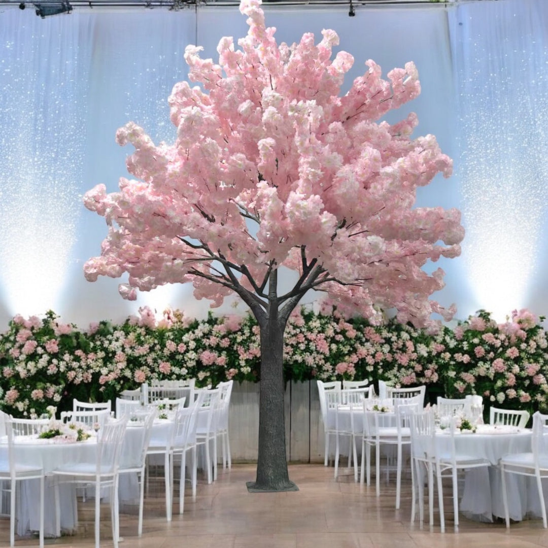 A large artificial pink cherry blossom tree placed in an elegant event space surrounded by white chairs and floral decorations. Is this tree suitable for both indoor and outdoor events?