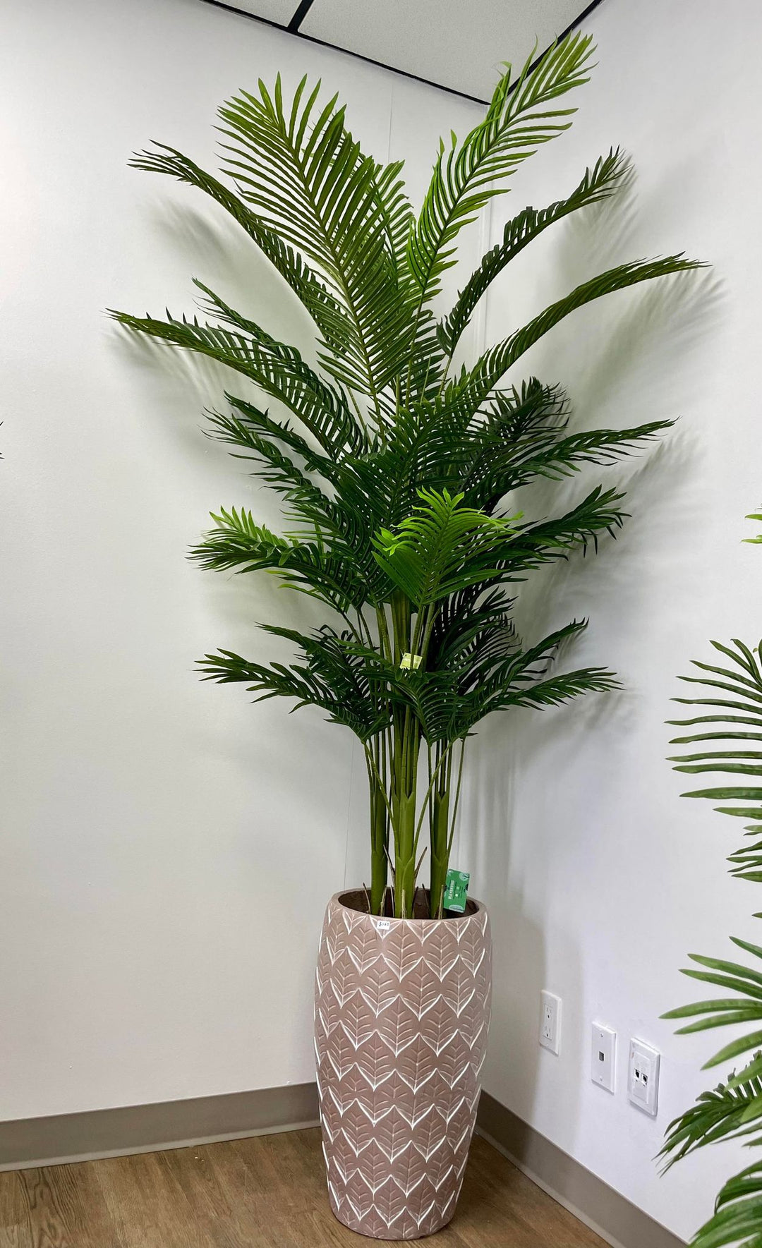 An artificial palm tree placed in a tall beige planter with white leaf patterns. The arrangement adds a touch of nature and elegance to the minimalist space.