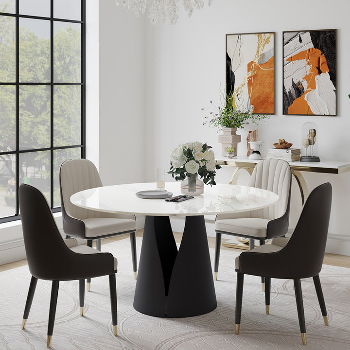 Chic round dining table with a polished marble top, complemented by four upholstered chairs in a modern dining room. The table features a tasteful floral centerpiece, while the room includes contemporary artwork and a decorative console table with various decor items. Large windows provide a view of the outdoors and flood the space with natural light, emphasizing the room's elegant and stylish design.