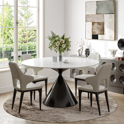 Stylish modern dining room with round white table, black tulip base, cream upholstered chairs, abstract art, decorative vases, floral arrangement, and view of greenery through large windows.