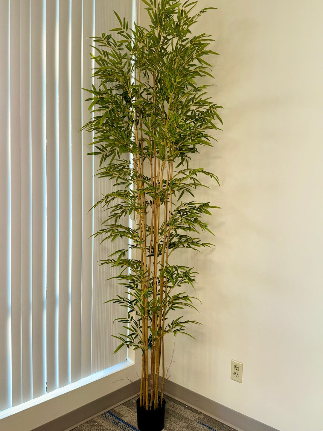 Full-height artificial bamboo tree placed in a modern interior corner, showcasing layered green leaves and natural bamboo trunks reaching toward the ceiling.