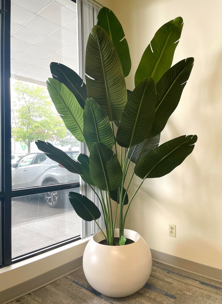 An 8-foot-tall artificial Bird of Paradise plant with large lush green leaves, placed in a white pot.