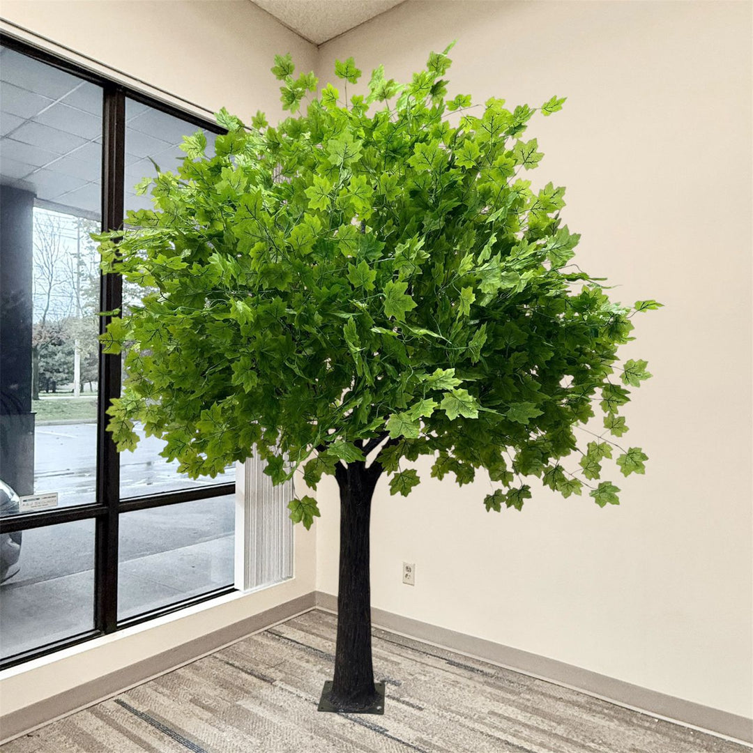 8ft artificial maple tree with lush green leaves and a dark brown trunk, displayed indoors in a room corner next to a window.