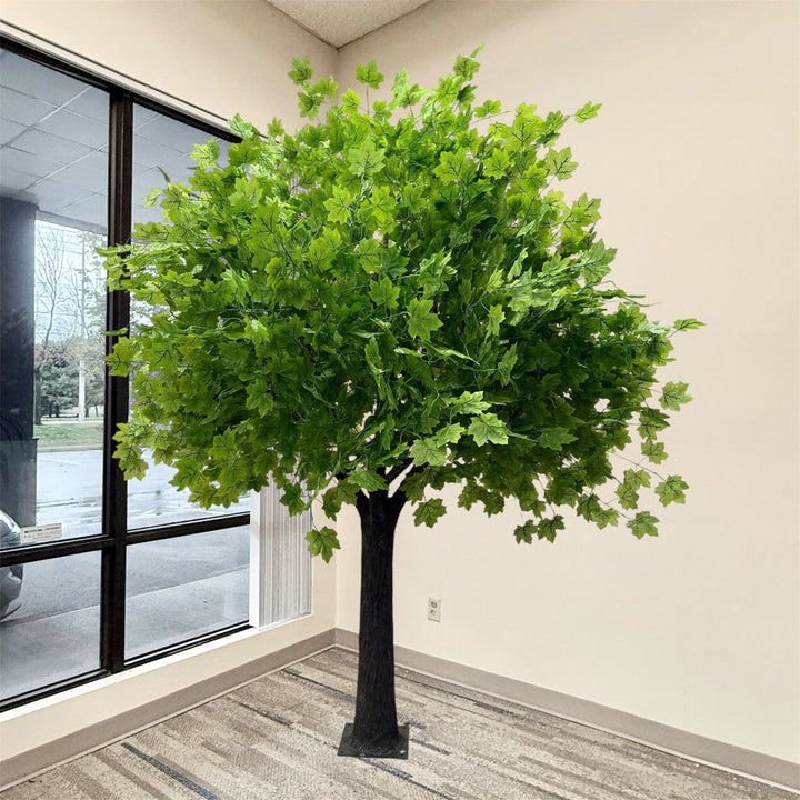 8ft artificial maple tree with lush green leaves and a dark brown trunk, displayed indoors in a room corner next to a window.