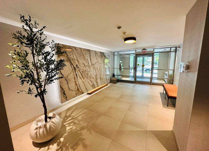 A modern lobby area featuring a large artificial olive tree in a stylish white planter.