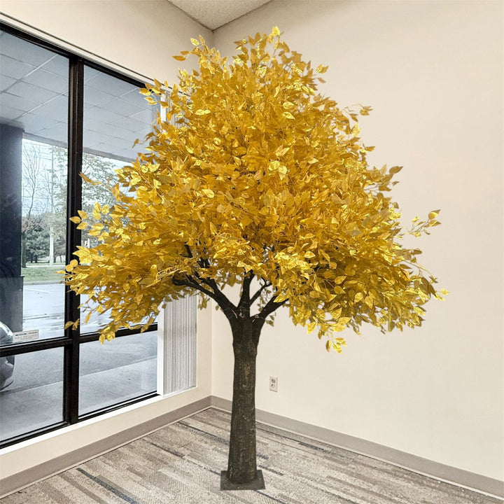 A 8ft artificial gold-colored ficus tree with metallic-looking leaves and a dark brown trunk, standing indoors near a window in a room with beige walls and gray patterned carpet.