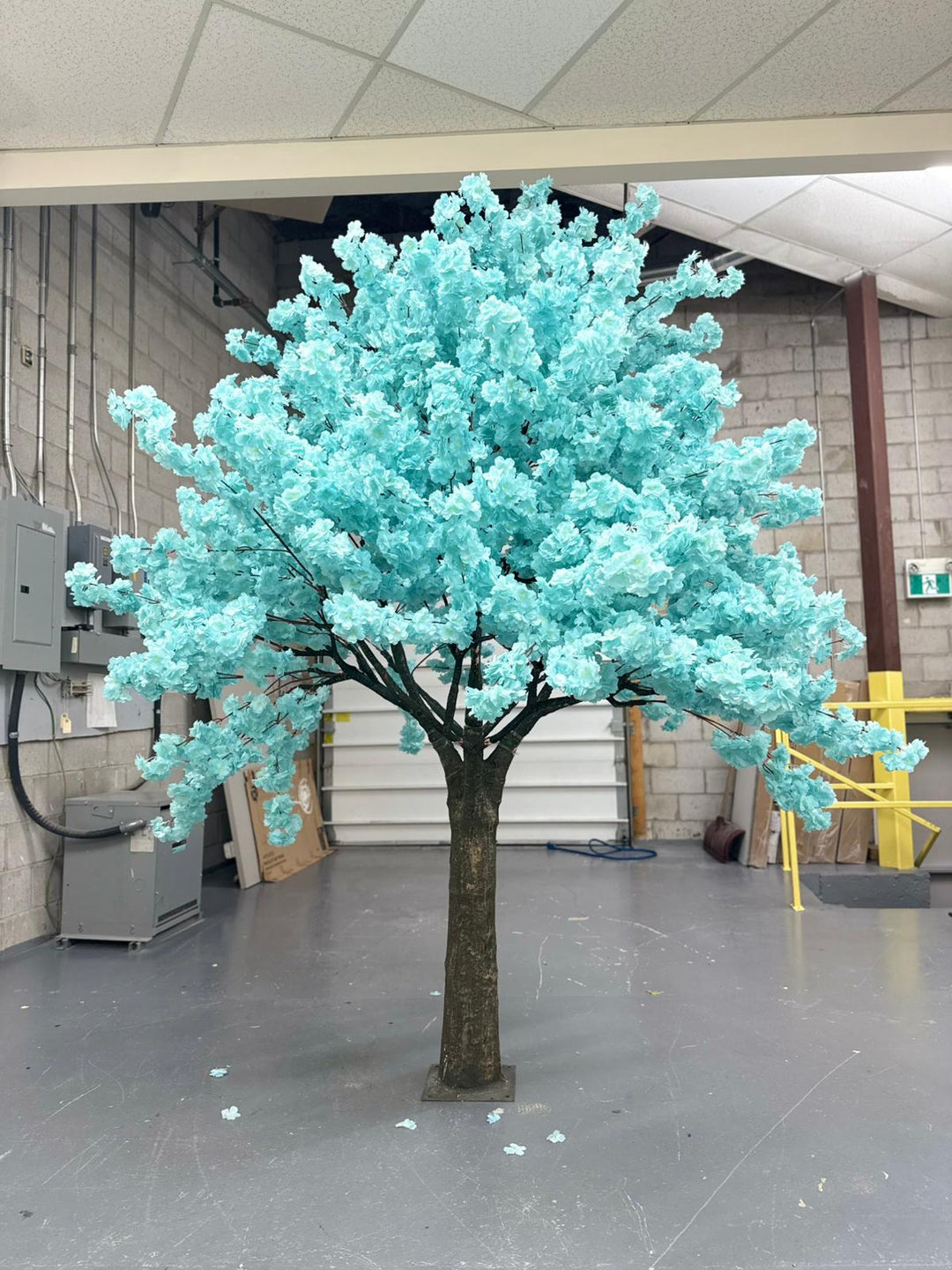 Artificial soft blue cherry blossom tree with turquoise leaves in a warehouse setting