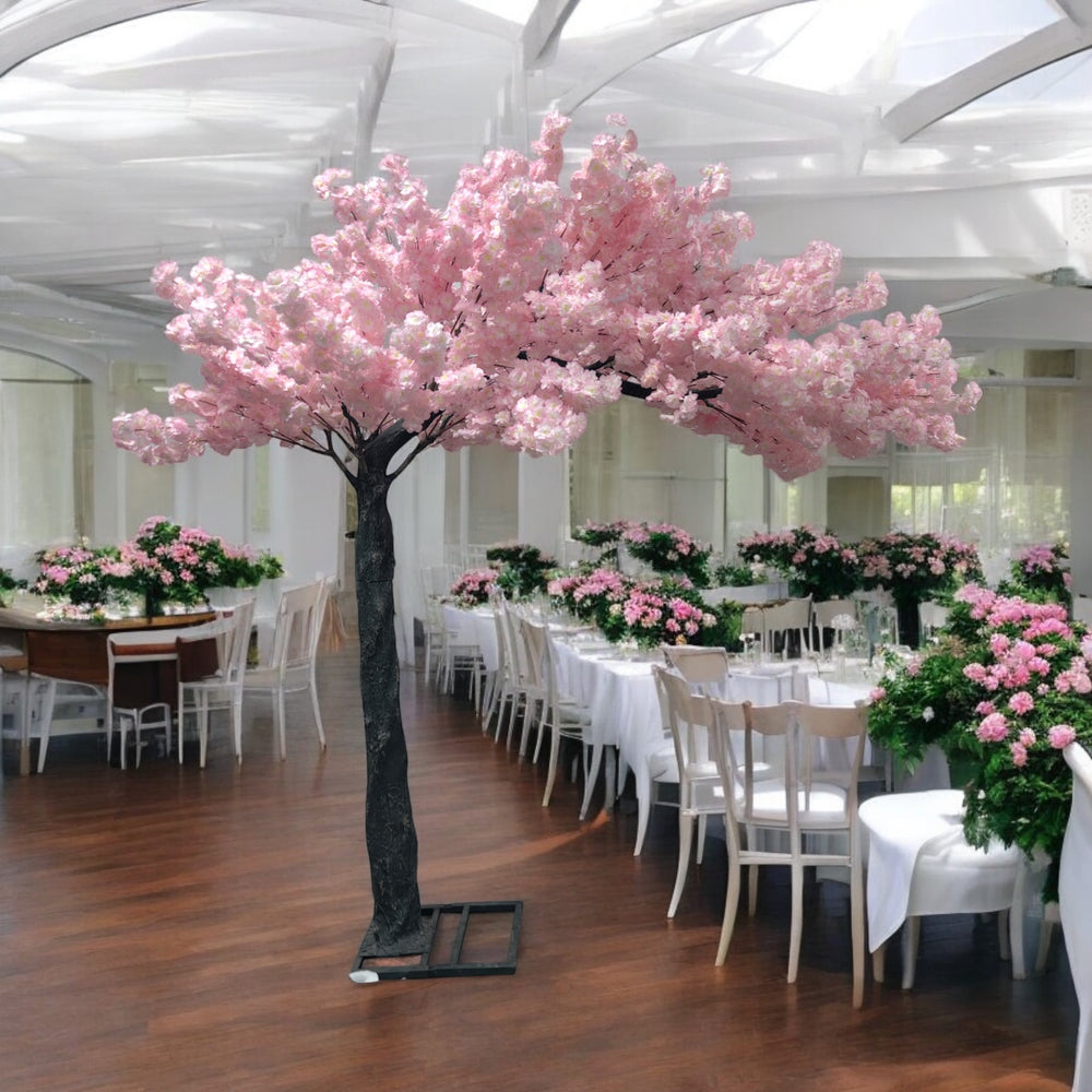 Elegant artificial arch cherry blossom tree with pink flowers, perfectly placed amidst a lavishly decorated wedding venue featuring pink floral arrangements and cascading fairy lights.