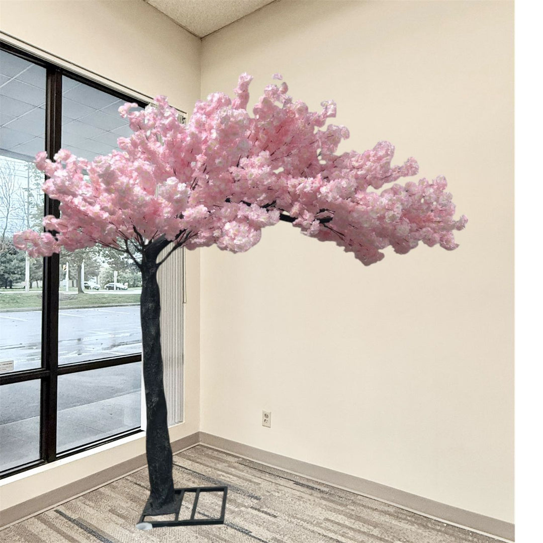 An artificial arch pink cherry blossom tree with dense pink blossoms and a dark trunk, displayed indoors near a large window on a carpeted floor.