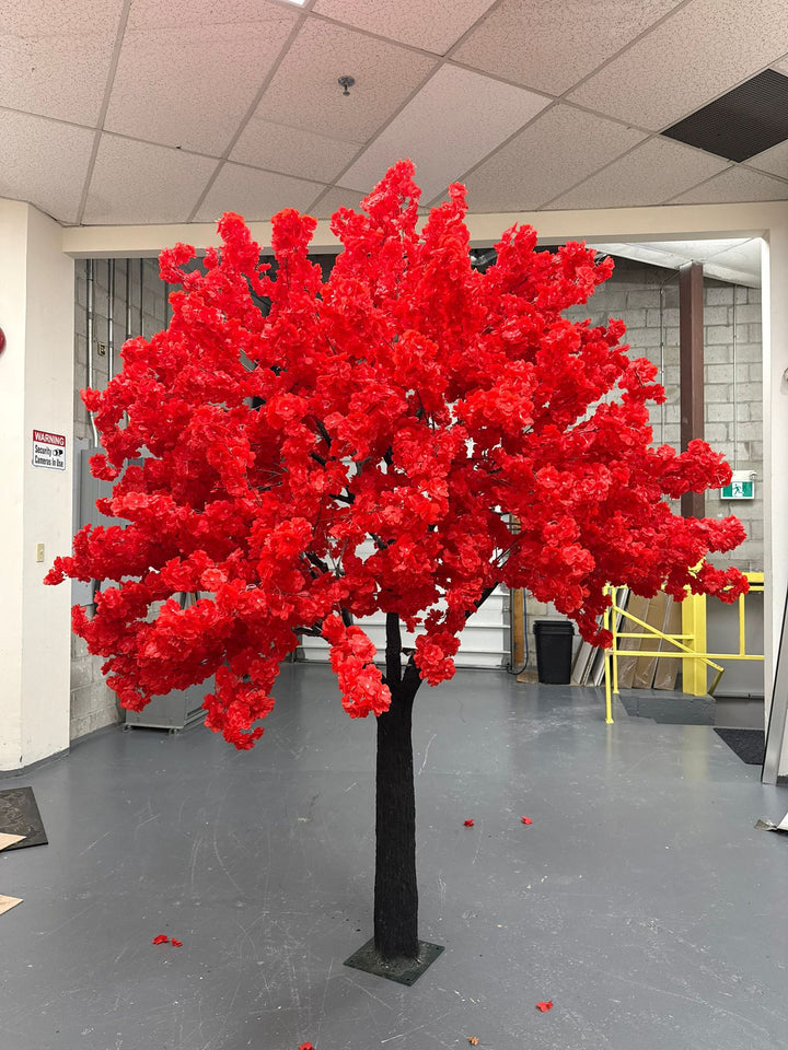 Red artificial cherry blossom tree in an indoor setting with a gray floor and white walls.