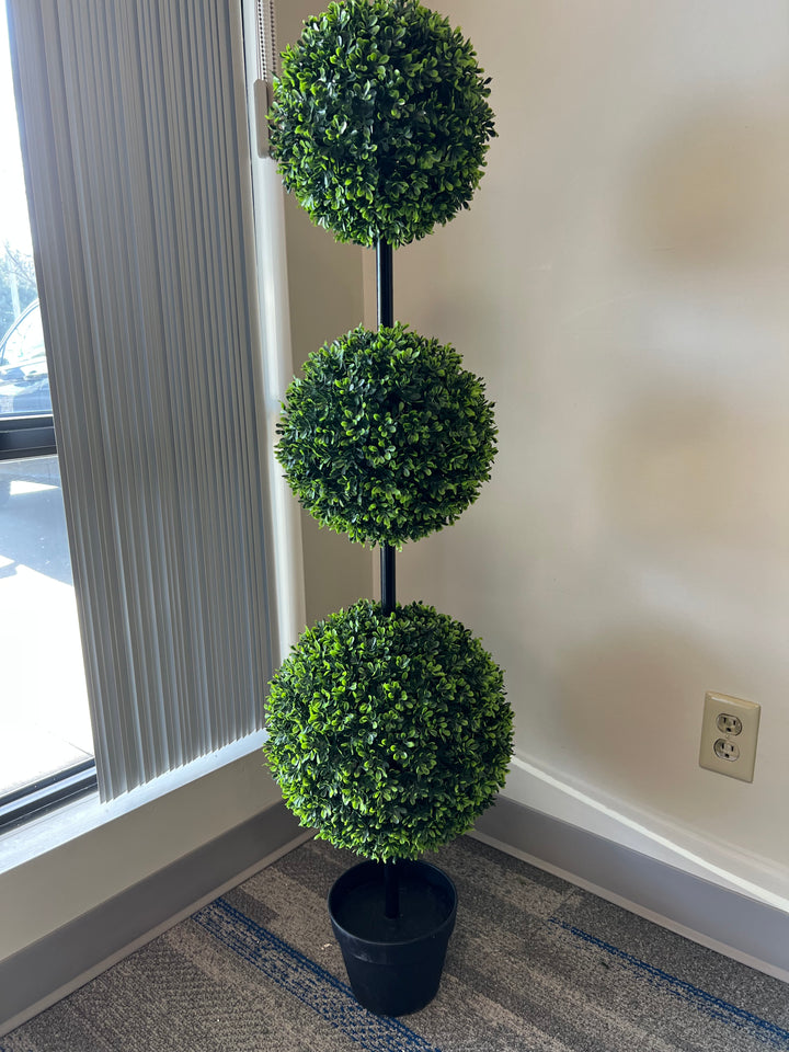 three-tier artificial topiary tree in a black planter next to a beautiful window perfect for enhancing indoor spaces with a touch of greenery and style.