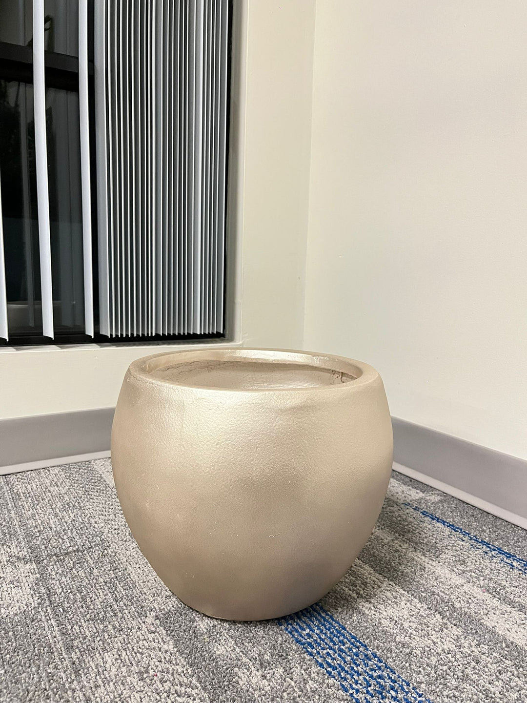 Gold cement round planter with a smooth finish placed indoors near a window. Does the planter have a scratch-resistant coating?