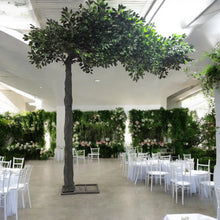 Charger l&#39;image dans la galerie, Artificial green tree with dense foliage, elegantly set in a wedding venue adorned with white round tables and a lush floral backdrop. This decoration adds a natural and sophisticated touch to your special day. Are these trees customizable for specific event themes?
