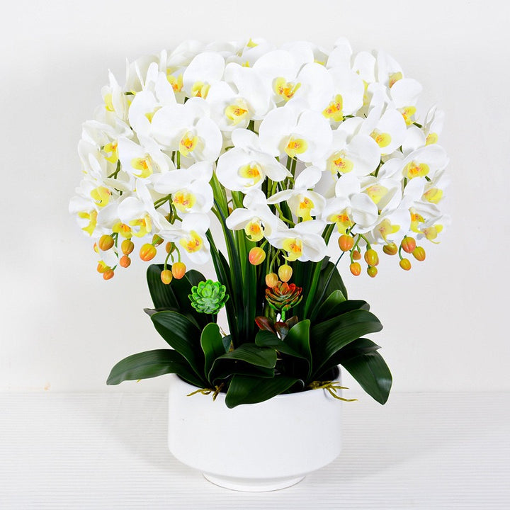 A large arrangement of artificial white orchids with lush green leaves in a modern white planter. Frequently asked question: What are the best planters to use for artificial plants to enhance their aesthetic appeal?