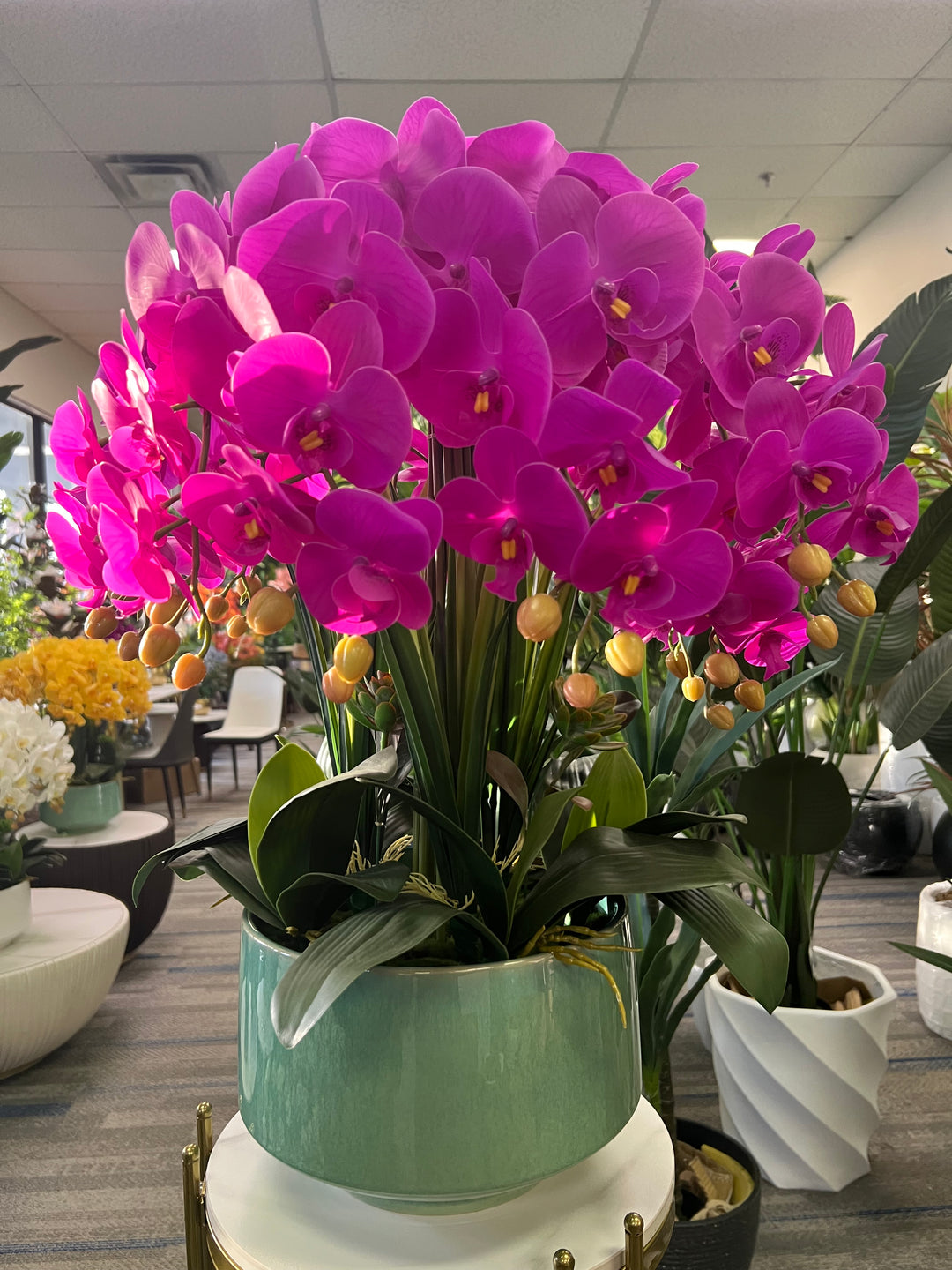 A vibrant artificial orchid arrangement in a bright fuchsia color, displayed in a modern white planter. Frequently asked question: How do I maintain artificial orchids to keep them looking fresh and dust-free?