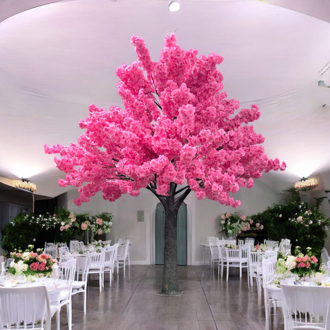 A vibrant artificial dark pink blossom tree standing in a spacious, elegant hall with white chairs and floral decorations, ideal for weddings or luxury events. 