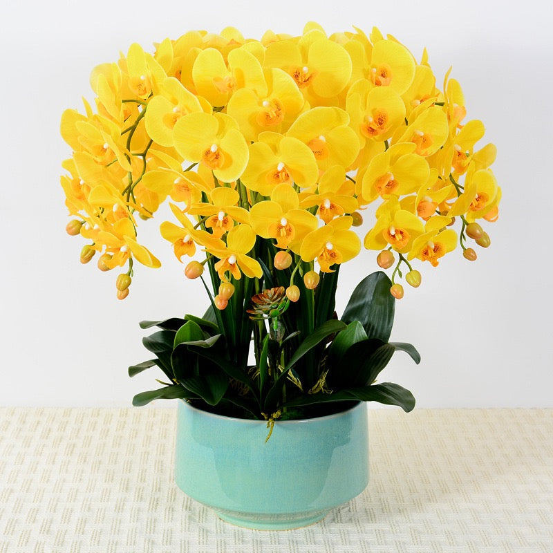 A vibrant arrangement of artificial yellow orchids with realistic petals and buds, displayed in a white ceramic pot. How can I keep artificial flowers looking fresh over time?