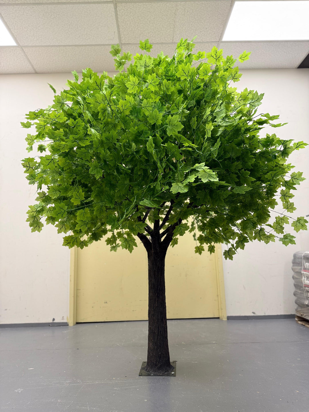 Artificial Green Maple Tree with realistic trunk and foliage stored in a warehouse.
