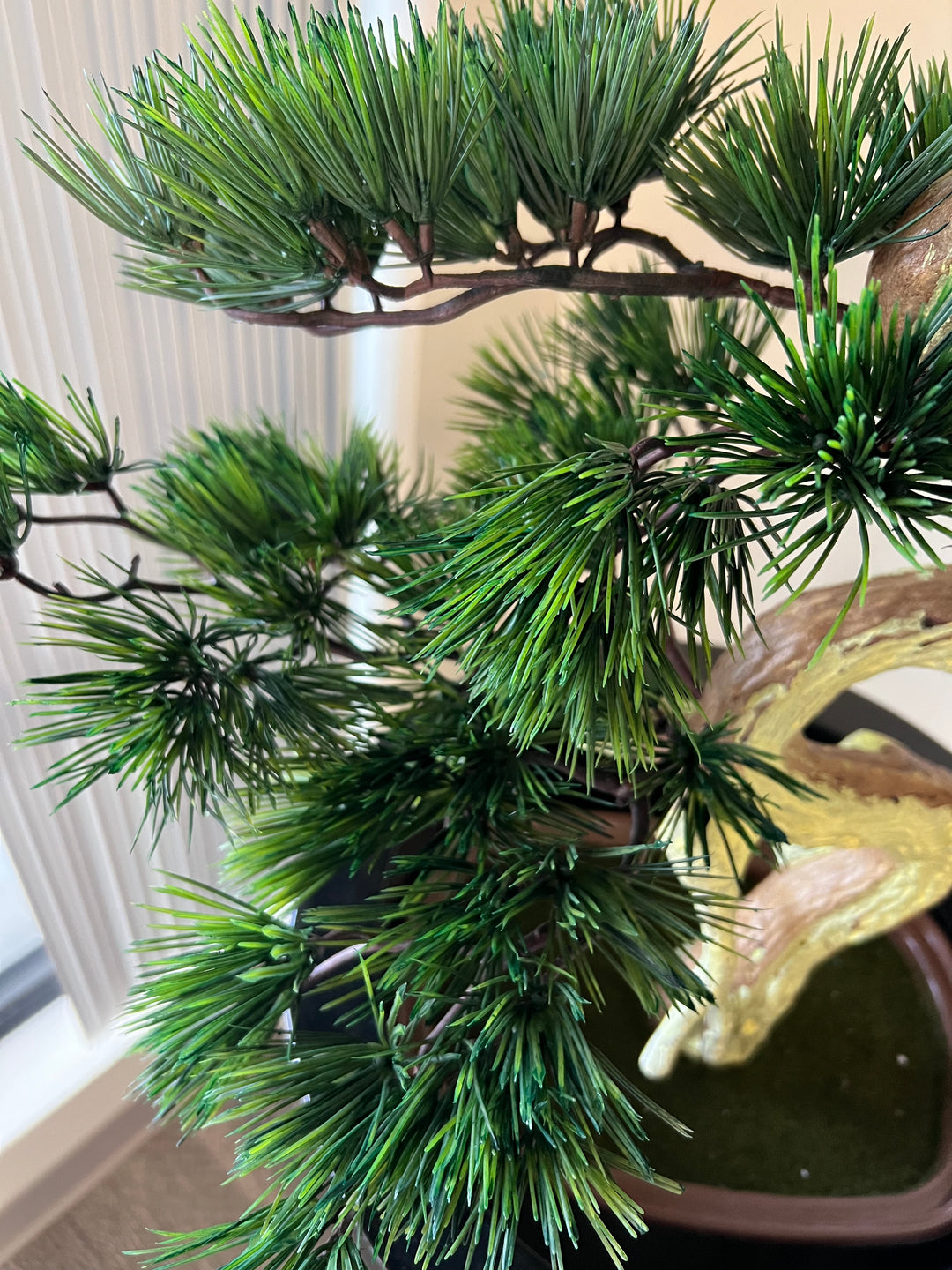 Close-up view of artificial bonsai tree branches with lush, needle-like green foliage, showcasing intricate details and texture of the leaves