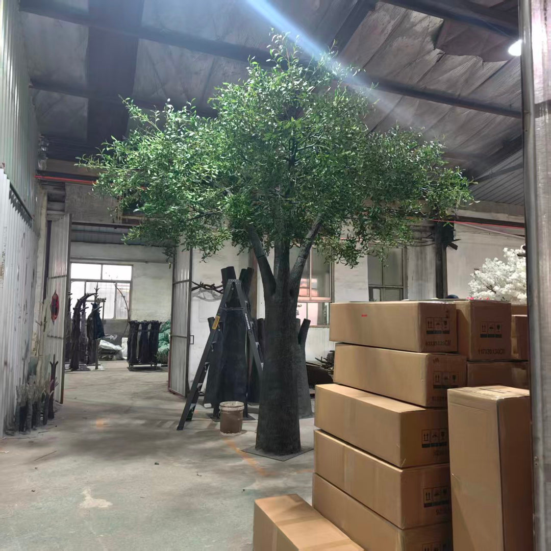 Indoor setting with 15ft artificial olive tree and stacked cardboard boxes in a warehouse.