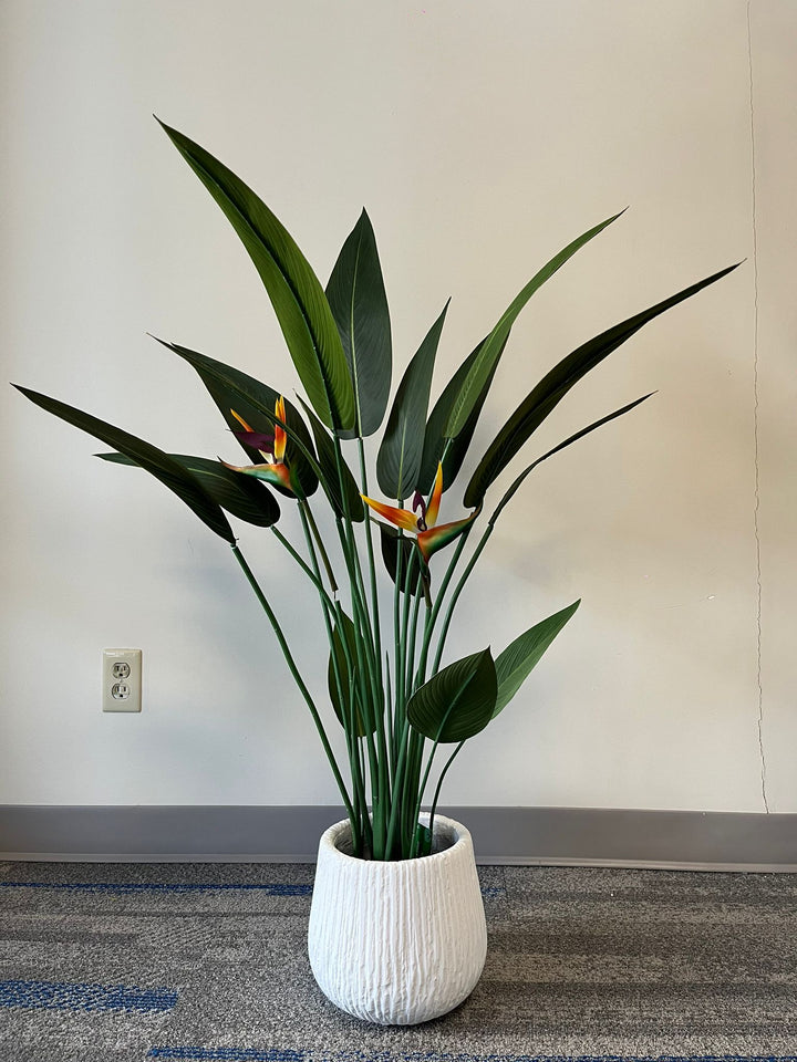 White textured planter with a ribbed design, holding a vibrant artificial bird of paradise plant with tall green leaves and orange flowers, placed indoors against a neutral background. Is this planter available in multiple sizes?