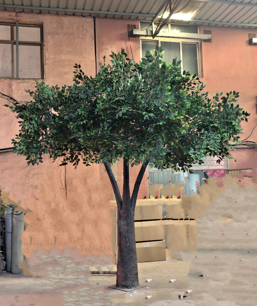 Artificial tree with a lifelike trunk and lush green foliage, displayed in an industrial outdoor setting, showcasing its durability and versatility for wedding and event decor. Are these rental trees suitable for both indoor and outdoor events?