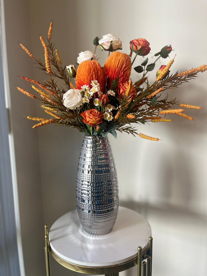 Autumn-inspired artificial floral arrangement with orange and cream flowers on a modern side table.