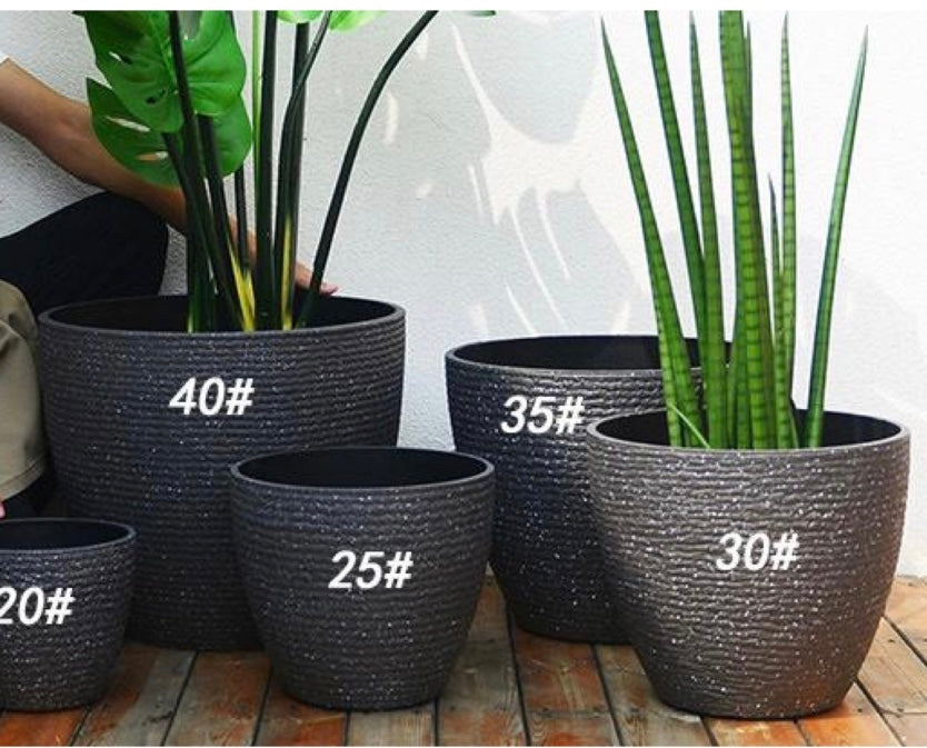 A collection of five textured black planters of varying sizes, labeled with numbers: 40#, 35#, 30#, 25#, and 20#. Each planter contains a different tall, leafy plant, displayed on a wooden deck against a white wall.