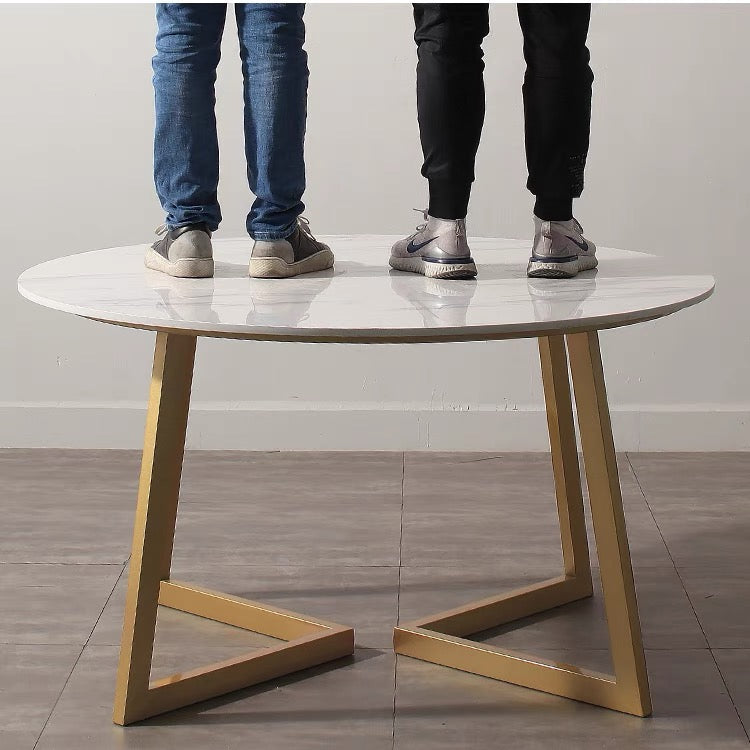 Sturdy round marble dining table with gold geometric base, demonstrating durability with two people standing on the tabletop, perfect for modern dining areas.