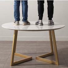 Load image into Gallery viewer, Sturdy Round Dining Table with a Glossy Sintered Stone Top and Robust Gold Metal Legs, Showcasing Strength with Two Individuals Standing on the Surface
