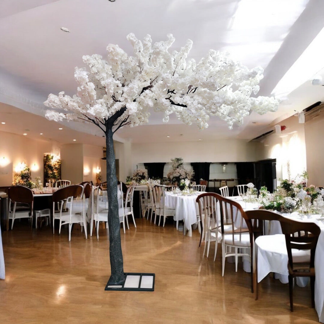 A luxurious indoor wedding venue decorated with a stunning artificial white cherry blossom tree centerpiece. The tree stands tall on a sturdy black base, blending beautifully with the elegant banquet setup, featuring white tablecloths and wooden chairs. How can I secure a decorative tree like this on a polished floor?