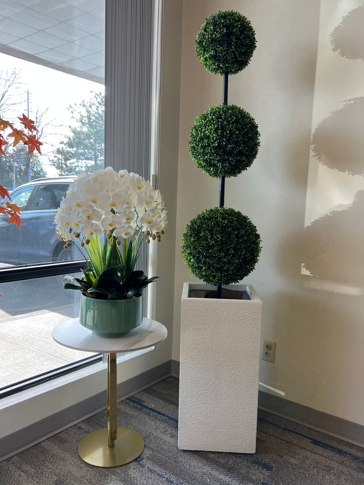 Elegant display of a three-tier artificial topiary tree in a modern white planter next to a beautiful white orchid arrangement, perfect for enhancing indoor spaces with a touch of greenery and style
